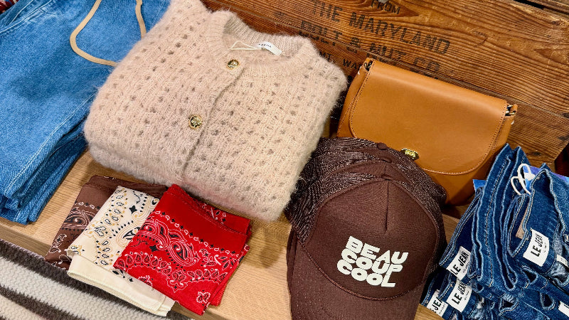 Display of clothing and accessories including jeans, sweaters, a cap, and bandanas on a wooden surface.