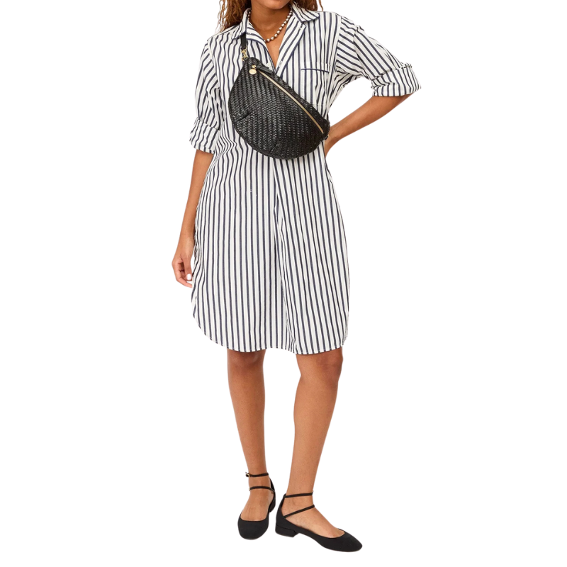 Woman wearing a black and white striped dress with a black crossbody bag on a white background