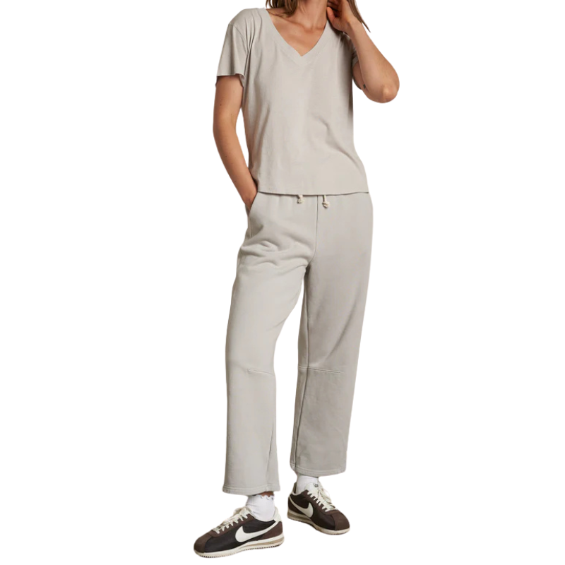 Person wearing a beige top and light gray pants with Nike shoes on a white background