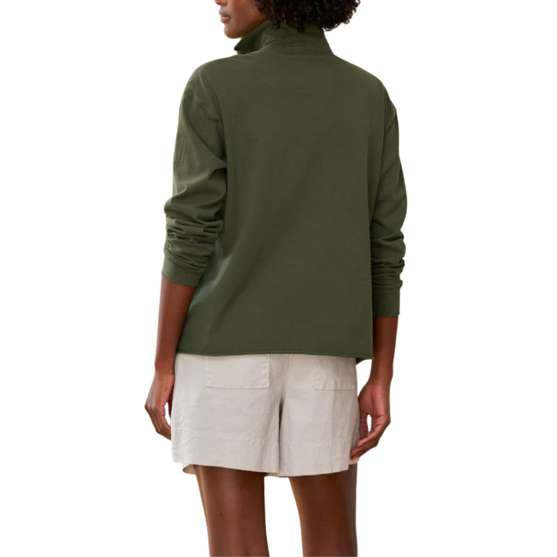 Person wearing a green turtleneck and beige shorts on a white background