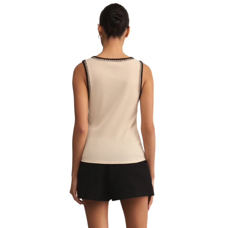 Woman wearing a beige sleeveless top with black trim and black shorts on a white background