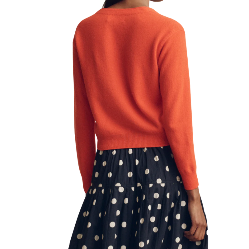 Person wearing an orange sweater and navy skirt with white polka dots on a white background