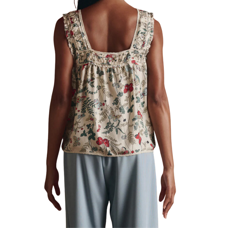 Woman wearing a floral sleeveless top and light gray pants on a white background