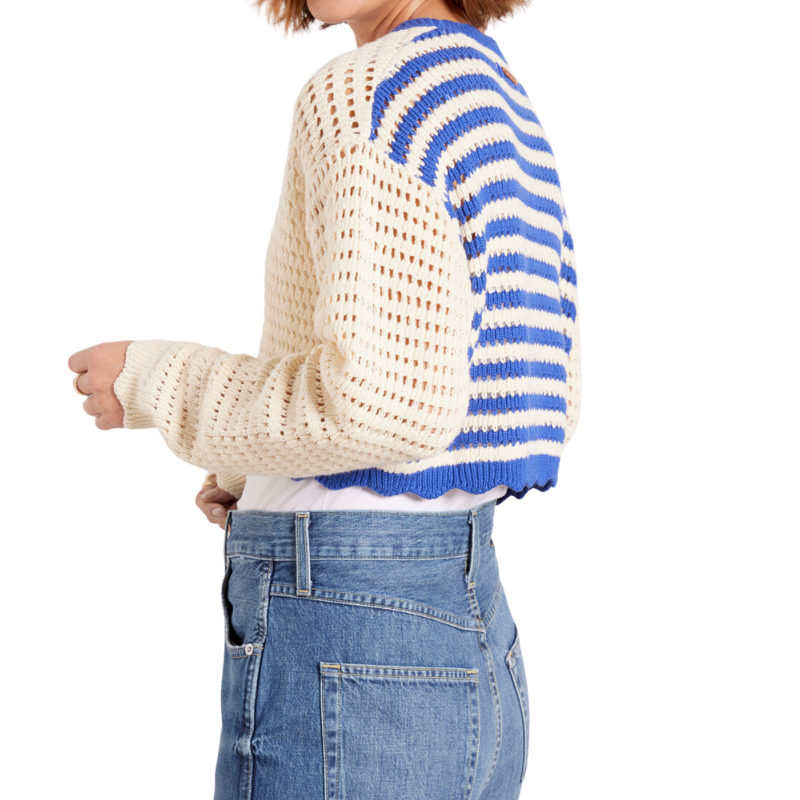 Person wearing a white and blue striped sweater with openwork design, standing against a white background.