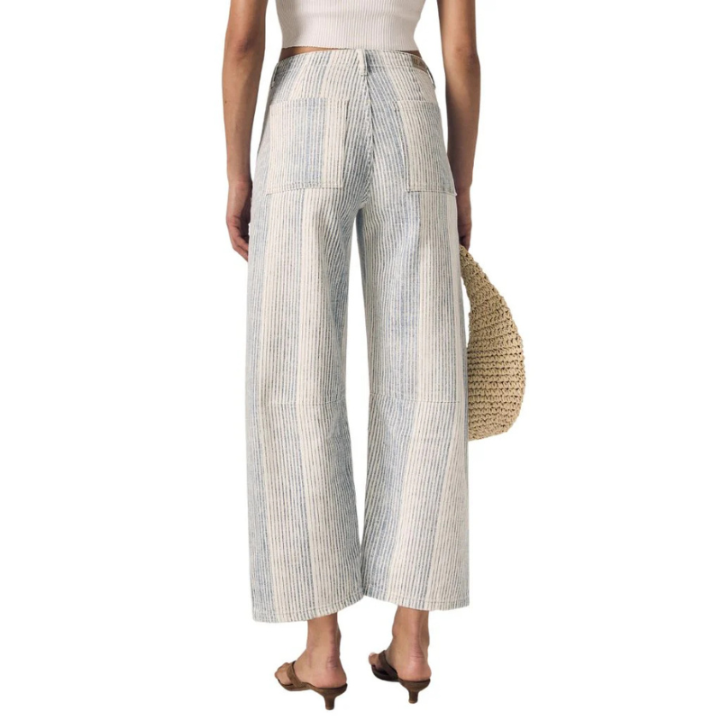 Person wearing striped wide-leg pants holding a straw bag on a white background