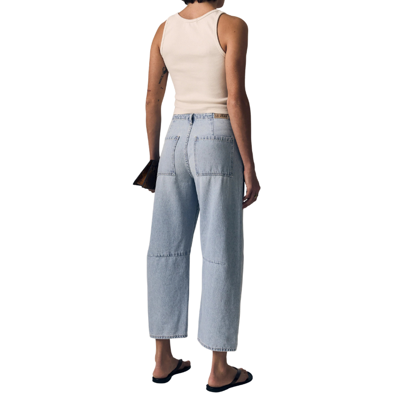 Person wearing light blue denim pants and a beige sleeveless top on a white background