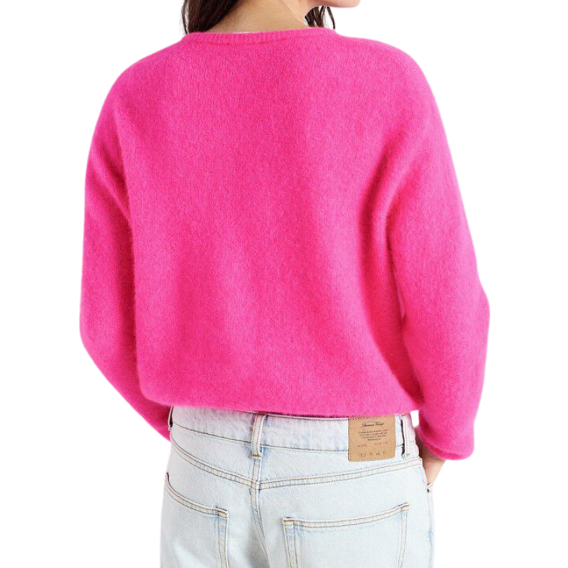 Person wearing a bright pink sweater and light blue jeans on a white background