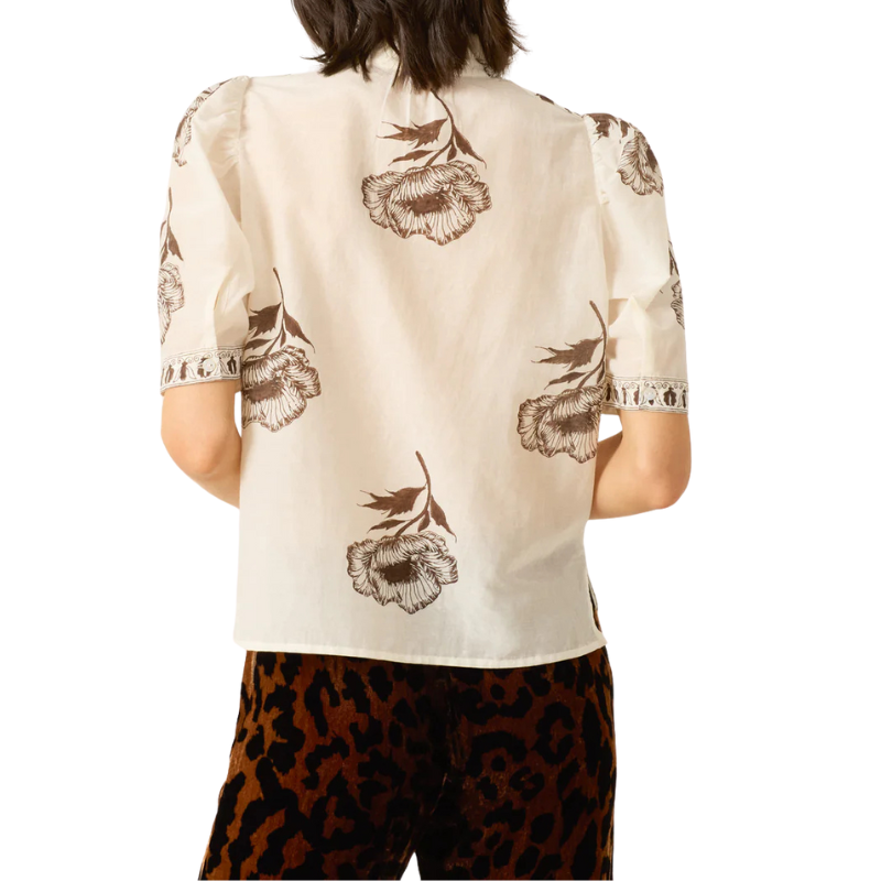 Person wearing a beige blouse with floral patterns and leopard print pants on a white background