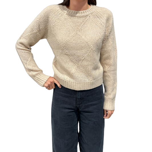 Person wearing a beige knitted sweater and dark pants on a white background