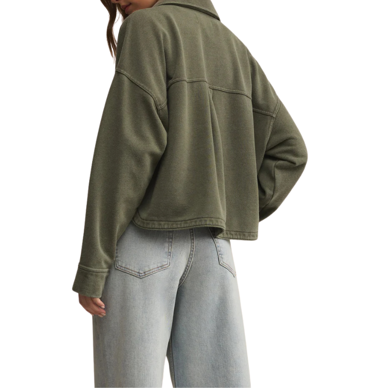 Person wearing an olive green jacket and light gray jeans on a white background