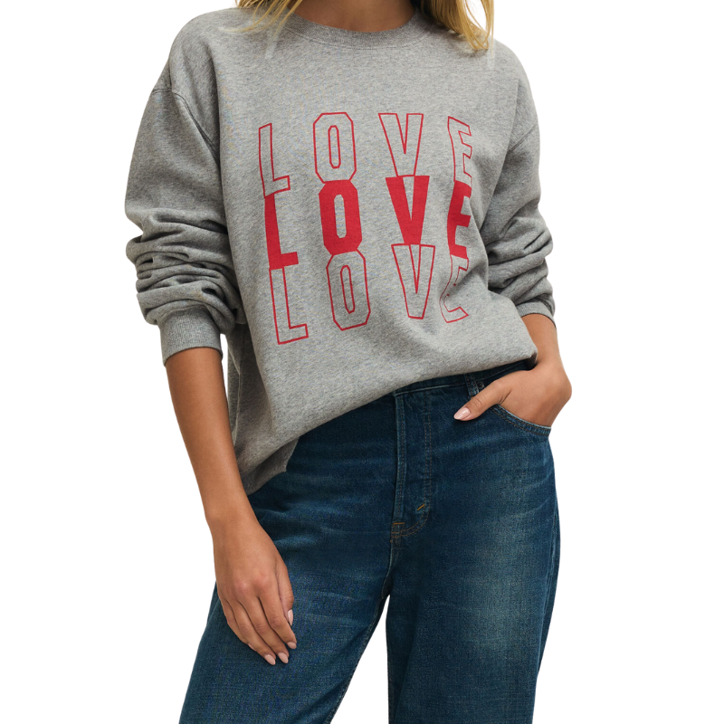 Person wearing a gray sweatshirt with 'LOVE' printed in red and blue jeans on a white background