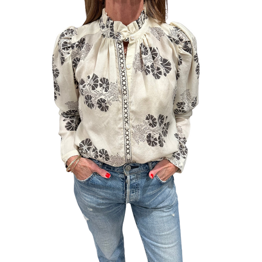 Woman wearing a white blouse with black floral patterns and blue jeans on a white background