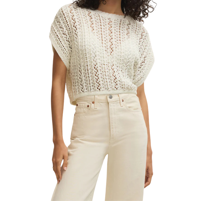 Person wearing a white crochet top and beige pants on a white background