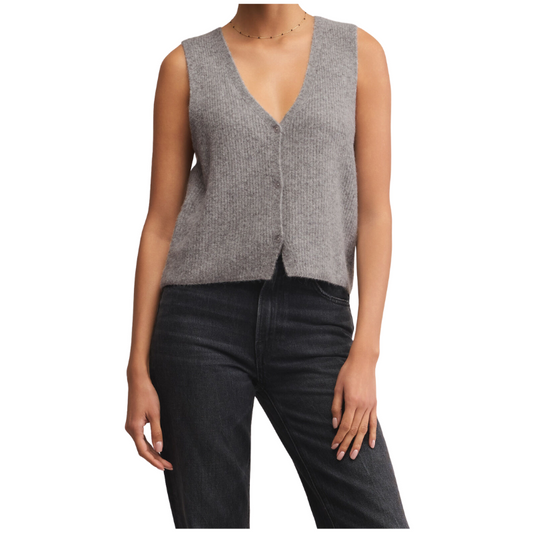 Woman wearing a gray sleeveless sweater vest and black jeans on a white background