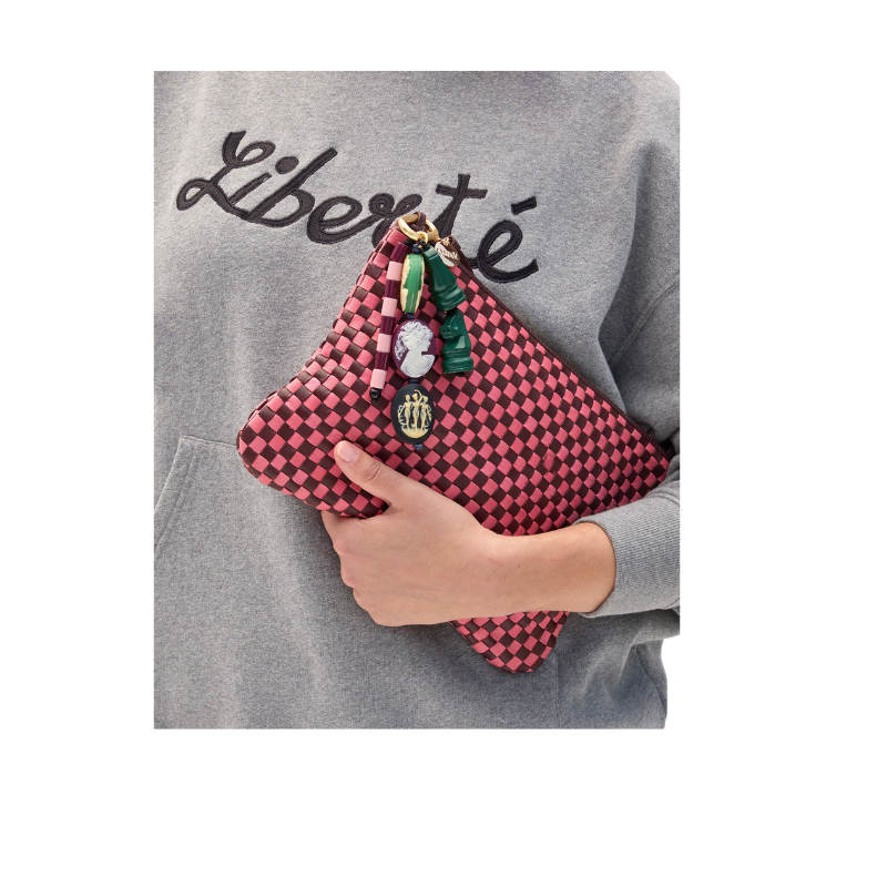 Person holding a pink checkered clutch with decorative elements against a gray sweatshirt background.
