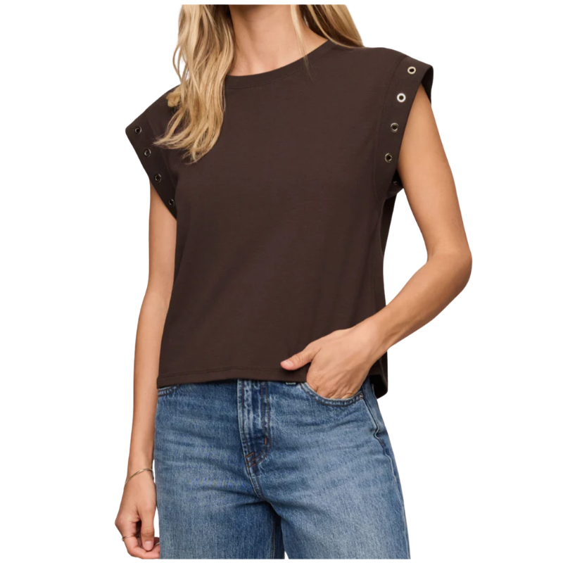 A woman wearing a dark brown sleeveless crop top with silver grommet details on the shoulders, paired with blue jeans, shown against a plain white background.