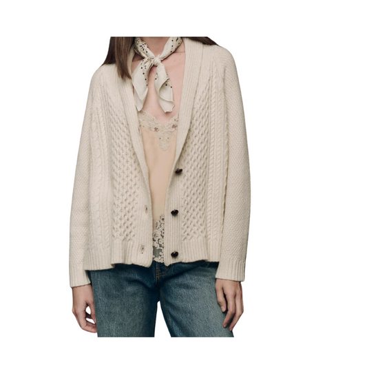 Person wearing a beige cable knit cardigan over a lace top and jeans on a white background