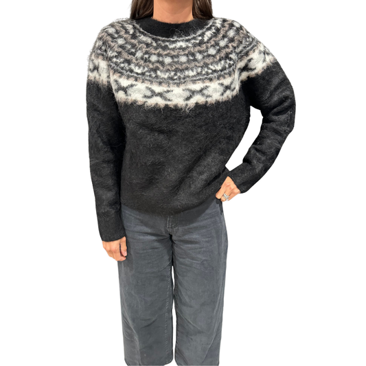 Person wearing a black and white patterned sweater with gray pants on a white background