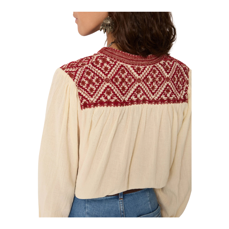 Beige blouse with red and white patterned yoke worn by a person on a white background