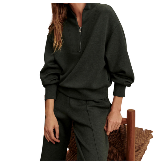 Person wearing a dark green zip-up sweatshirt and pants sitting on a wooden chair.