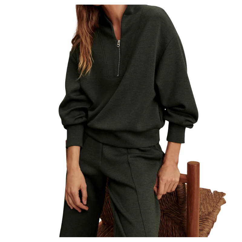 Person wearing a dark green zip-up sweatshirt and pants sitting on a wooden chair.