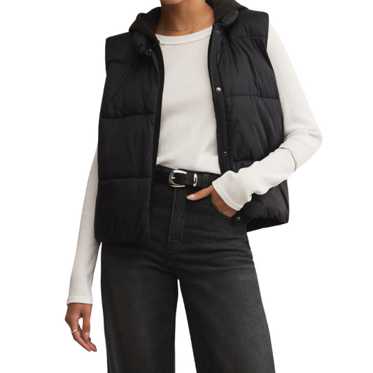 Person wearing a black puffer vest over a white long-sleeve shirt with black pants on a white background