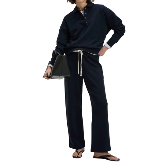 Person wearing a navy blue outfit with wide-leg pants and holding a black clutch on a white background