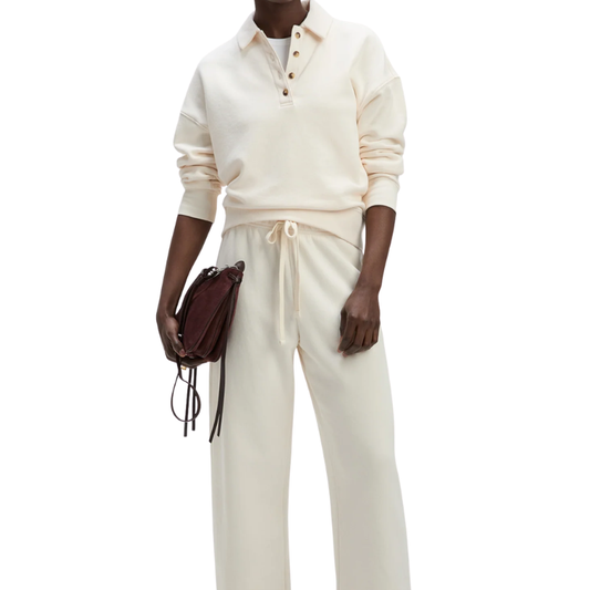 Person wearing a cream-colored outfit with a brown leather bag on a white background