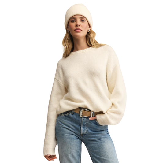 Woman wearing a cream sweater, beige beanie, and blue jeans on a white background