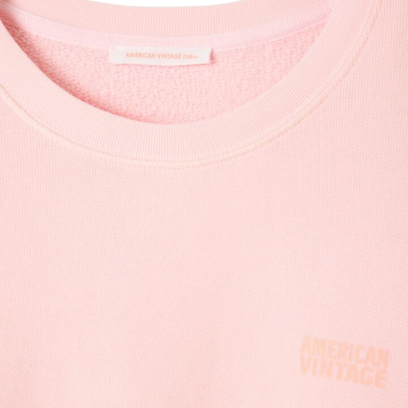 Close-up of a pink sweatshirt with a brand label on a light pink background