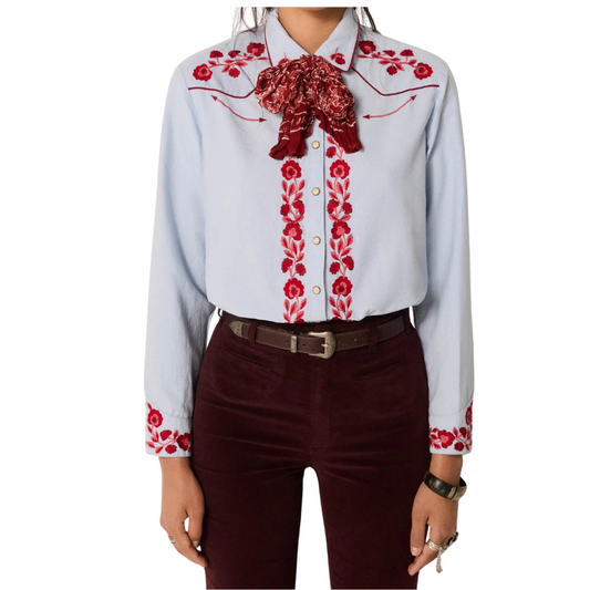 Light blue shirt with red floral embroidery and a red scarf, paired with dark pants on a white background.