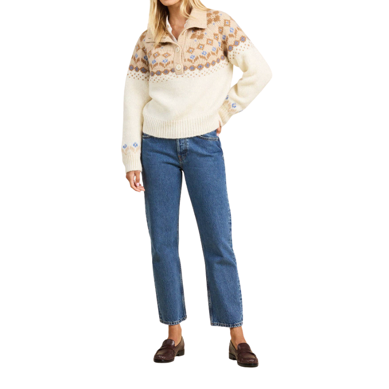 Person wearing a cream sweater with patterned sleeves and blue jeans on a white background