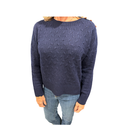 Person wearing a navy blue cable knit sweater and jeans on a white background