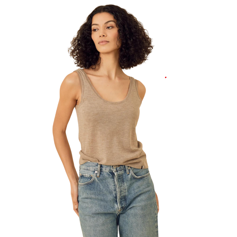 Woman wearing a beige tank top and blue jeans on a white background