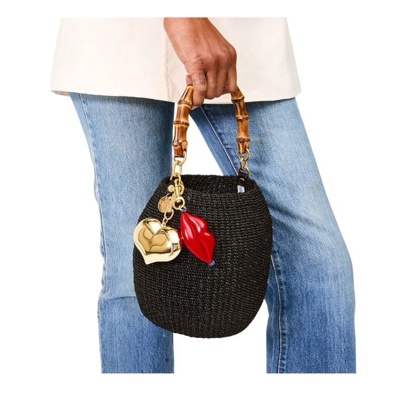 Black woven handbag with gold and red charm held by a person wearing blue jeans.