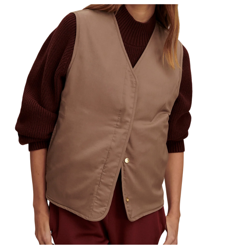 Person wearing a brown vest over a maroon sweater and pants on a white background