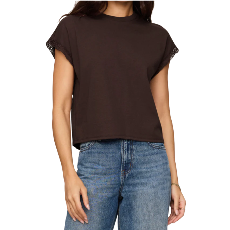 A woman wearing a dark brown short-sleeve crop top with lace trim on the sleeves, paired with blue jeans, against a plain white background.