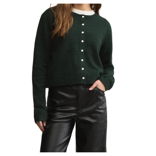 Person wearing a green cardigan with white buttons and black pants on a white background