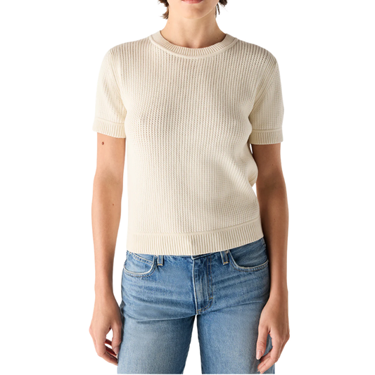 Person wearing a beige ribbed sweater and blue jeans on a white background