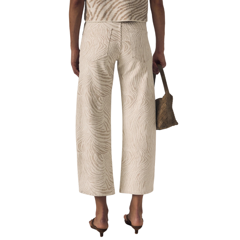 Person wearing patterned pants and a top, holding a bag on a white background