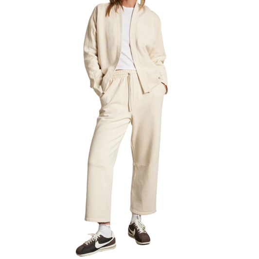 Person wearing a beige tracksuit with white sneakers on a white background