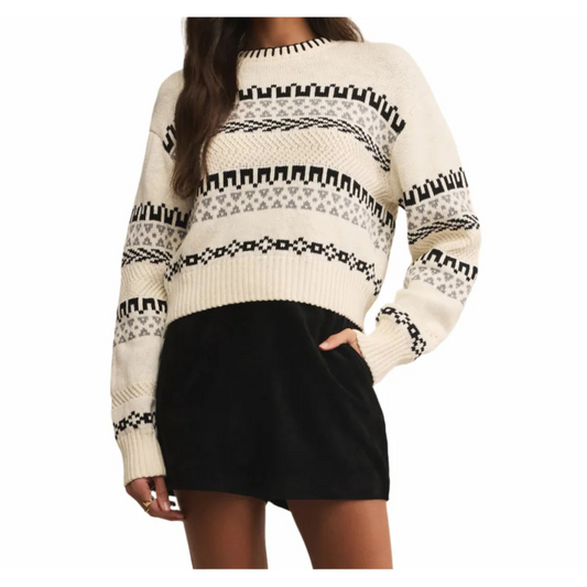 Person wearing a cream sweater with black pattern and black skirt on a white background