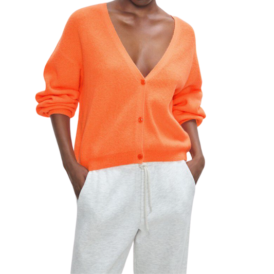 Person wearing an orange cardigan and gray pants on a white background