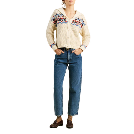 Person wearing a cream embroidered sweater and blue jeans on a white background