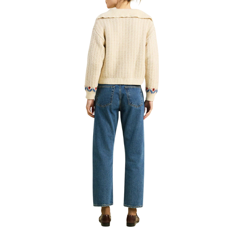 Person wearing a cream sweater and blue jeans on a white background