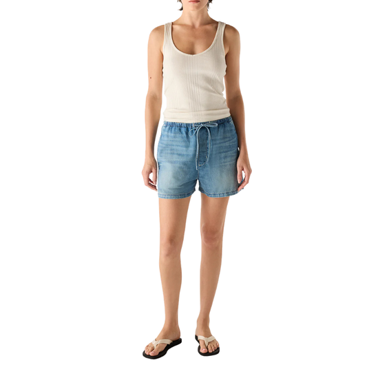 Person wearing a beige tank top and blue denim shorts on a white background