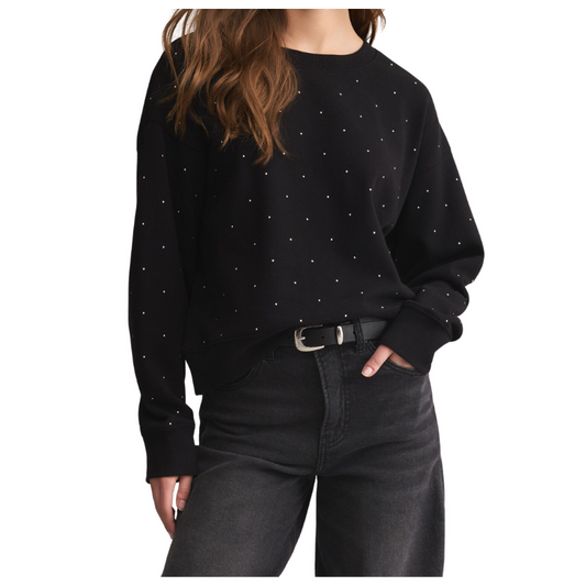 Person wearing a black sweater with white polka dots and dark jeans on a white background