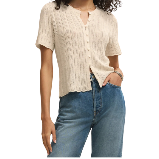 Woman wearing a beige ribbed sweater and blue jeans on a white background