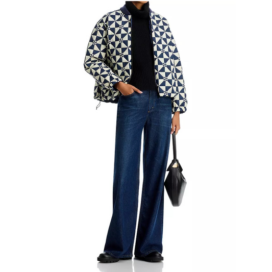 Person wearing a patterned jacket, black turtleneck, blue jeans, and holding a black handbag on a white background