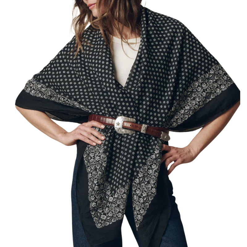 Woman wearing a black and white patterned poncho with a brown belt on a white background